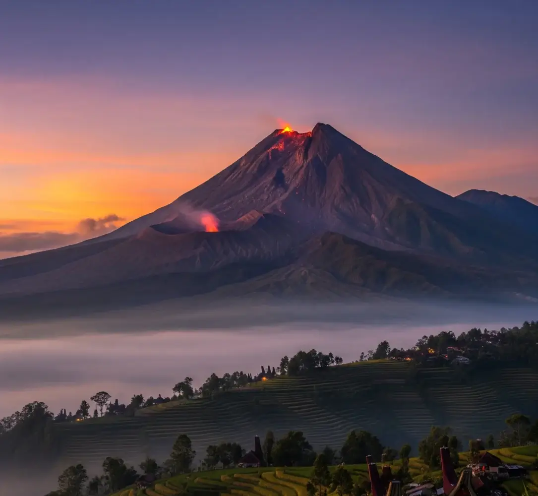 Pemandangan megah Gunung Merapi saat fajar, dengan puncak berkabut dan sedikit asap, melambangkan kekuatan alam dan aura mistis.